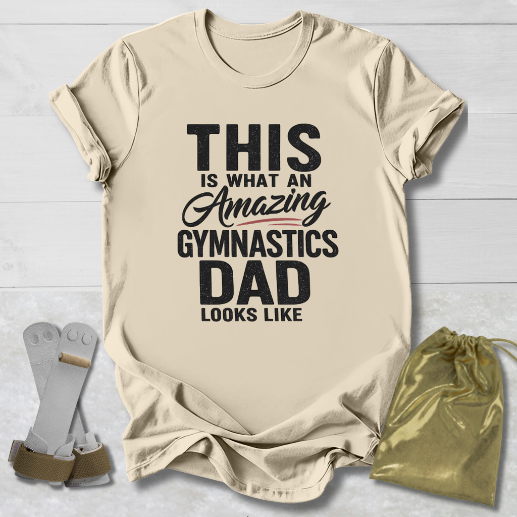 Beige t-shirt with text 'This is what an amazing gymnastics dad looks like' on a light wooden surface.
