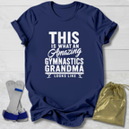 Navy blue t-shirt with white text 'This is what an amazing gymnastics grandma looks like' on a light wooden surface.