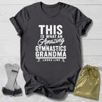 Gray t-shirt with 'Amazing Gymnastics Grandma' text on a light wooden surface with socks and a drawstring bag.