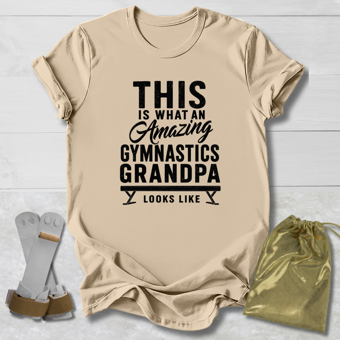 Beige t-shirt with black text 'This is what an amazing gymnastics grandpa looks like' on a light wooden surface.