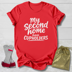 Red t-shirt with 'My second home has cupholders' text, socks, and drawstring bag on a light wooden surface.