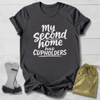 Dark gray t-shirt with 'My second home has cupholders' text, socks, and drawstring bag on a light wooden surface.