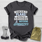 Dark gray t-shirt with text 'Weekend plans: spoiling my grandkids & watching gymnastics' on a light wooden surface.