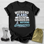 Black t-shirt with text 'Weekend plans: spoiling my grandkids & watching gymnastics' on a light wooden surface.