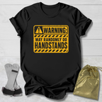 Black t-shirt with yellow warning sign graphic on a light wooden surface.