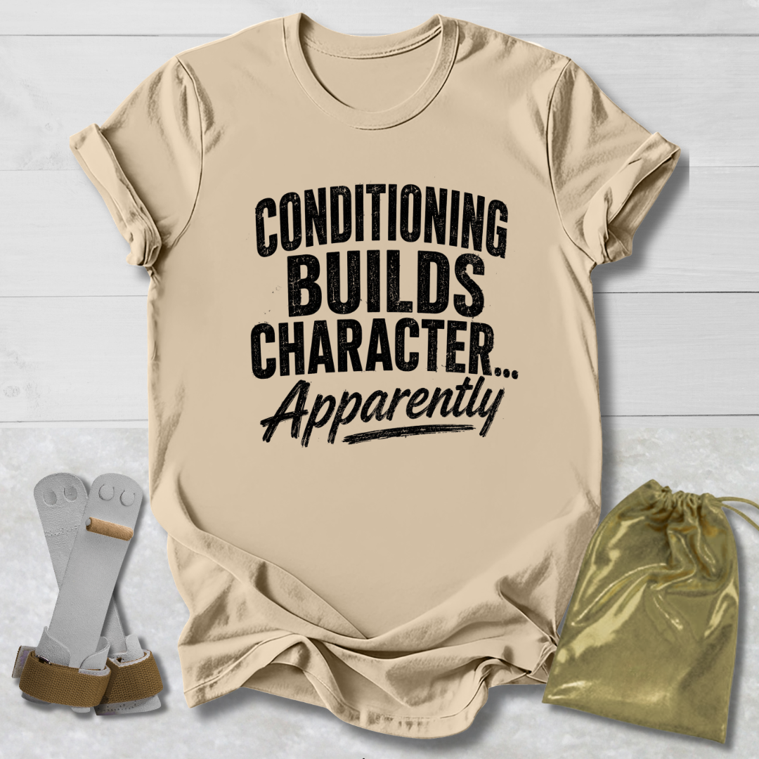 Beige t-shirt with text 'Conditioning Builds Character... Apparently' on a light wooden surface.