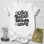 White t-shirt with 'Life's Better Upside Down' text on a light wooden surface with socks and a drawstring bag.