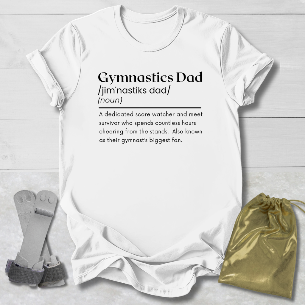 White t-shirt with 'Gymnastics Dad' definition text on a wooden surface with socks and a drawstring bag.