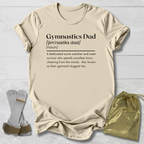 Beige t-shirt with 'Gymnastics Dad' definition text, socks, and drawstring bag on a light wooden surface.