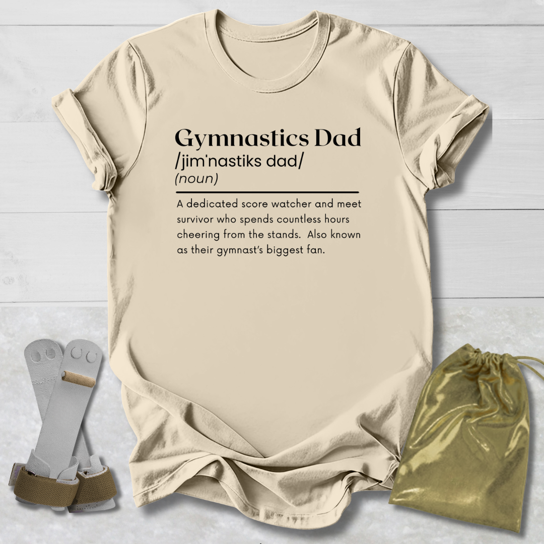 Beige t-shirt with 'Gymnastics Dad' definition text, socks, and drawstring bag on a light wooden surface.