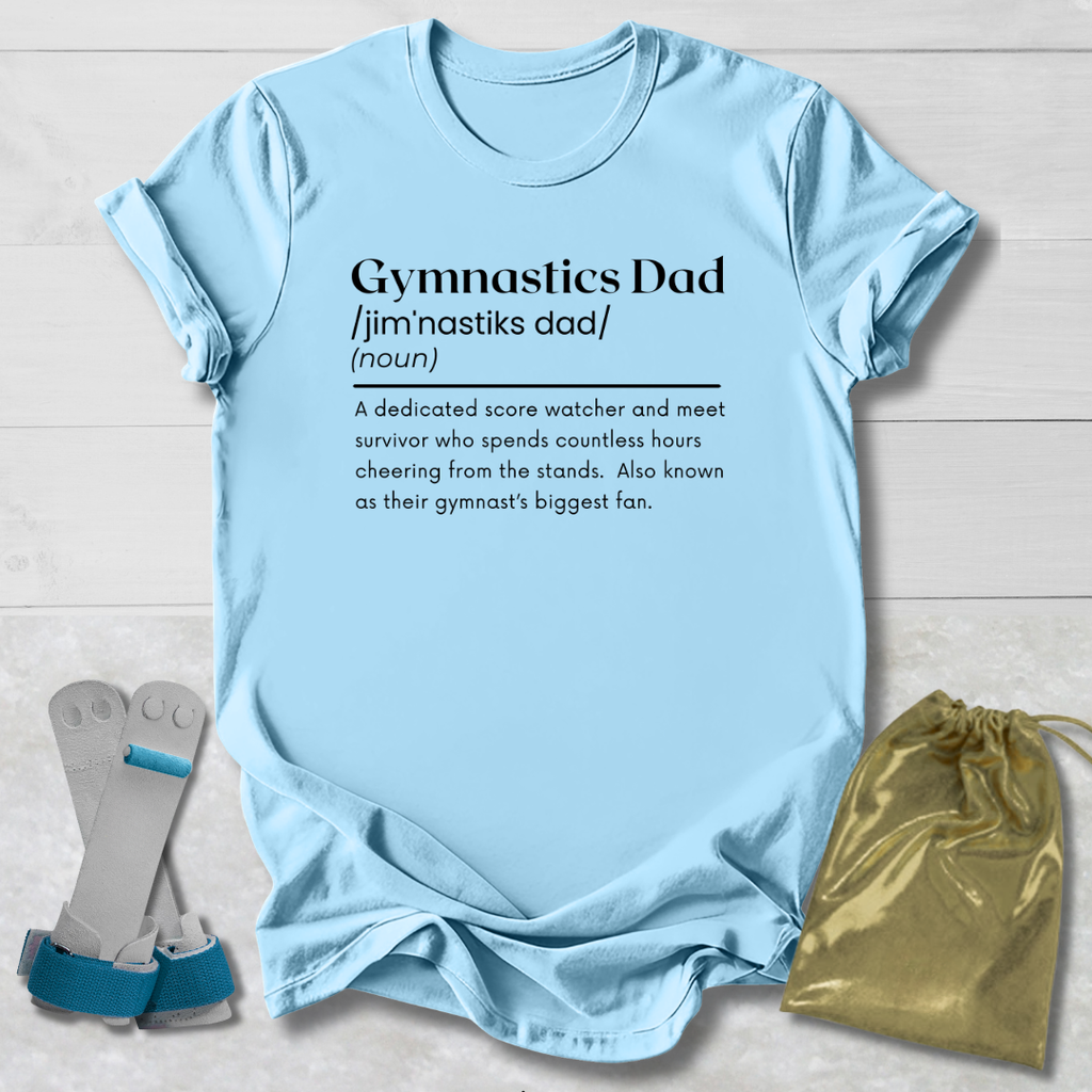 Light blue t-shirt with 'Gymnastics Dad' definition text, socks, and drawstring bag on a wooden surface.