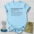 Light blue t-shirt with 'Gymnastics Dad' definition text, socks, and drawstring bag on a wooden surface.