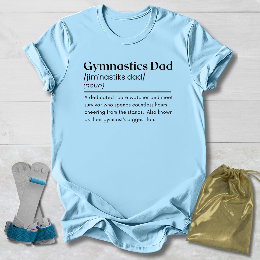 Light blue t-shirt with 'Gymnastics Dad' definition text, socks, and drawstring bag on a wooden surface.