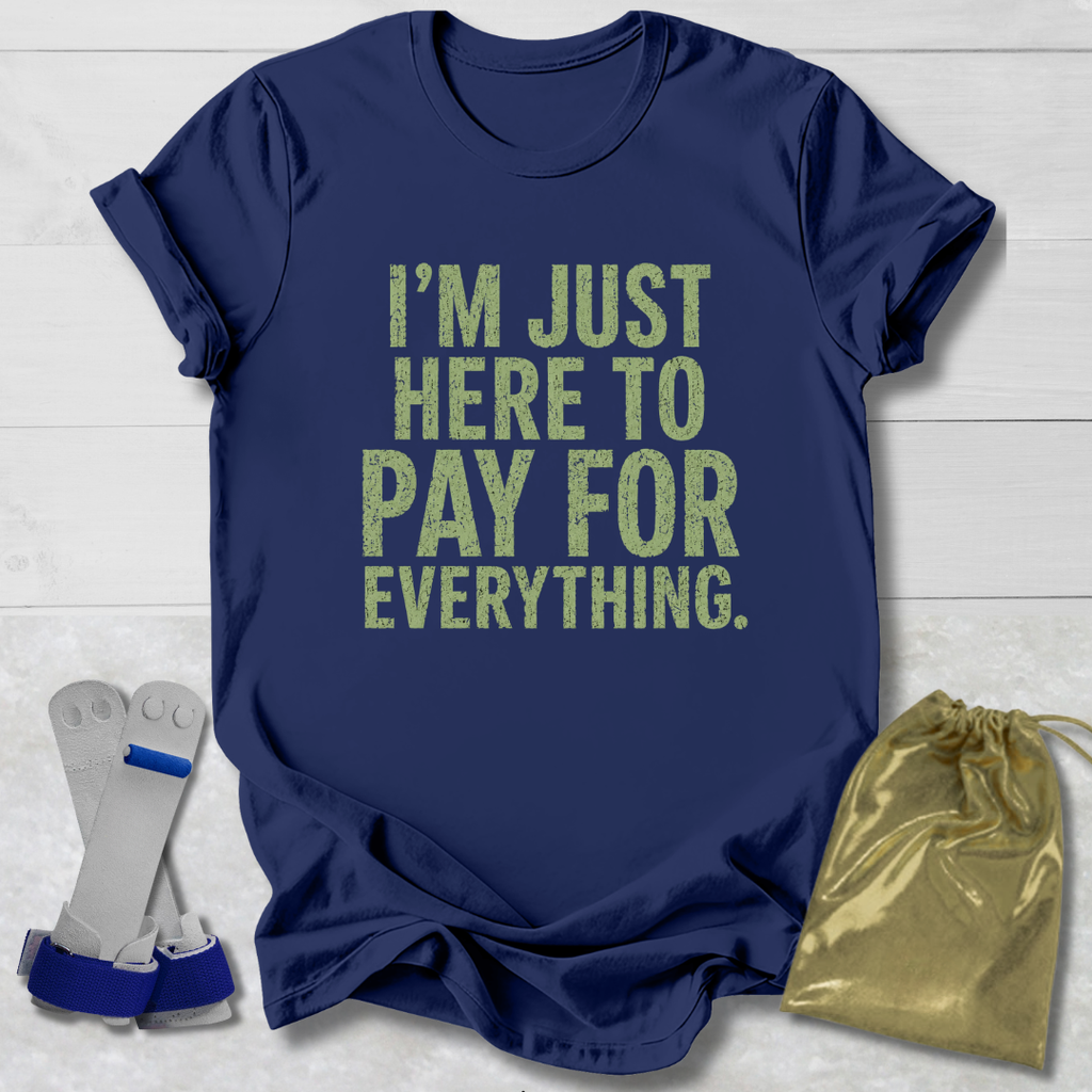 Navy blue t-shirt with yellow text 'I'm just here to pay for everything' on a light wooden surface.