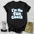 Black t-shirt with 'I'm the fun coach' text on a light wooden surface with socks and a drawstring bag.