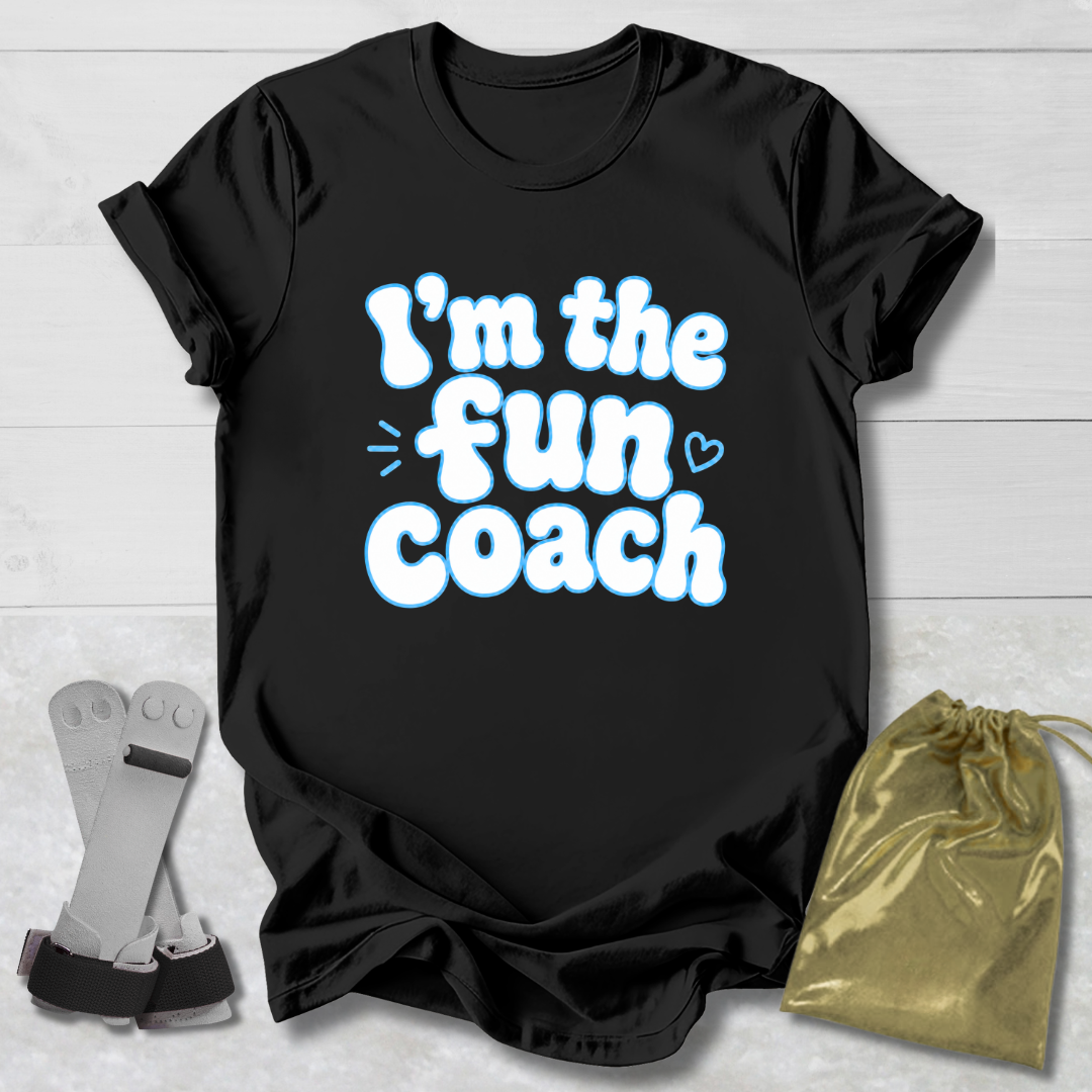 Black t-shirt with 'I'm the fun coach' text on a light wooden surface with socks and a drawstring bag.