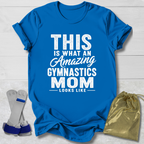 Blue t-shirt with 'Amazing Gymnastics Mom' text on a light wooden surface with socks and a drawstring bag.