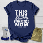 Navy blue t-shirt with white text 'This is what an amazing gymnastics mom looks like' on a light wooden surface.