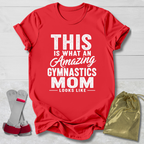 Red t-shirt with text 'This is what an amazing gymnastics mom looks like' on a light wooden surface, with socks and a drawstring bag.