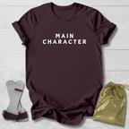 Maroon t-shirt with 'MAIN CHARACTER' text, socks, and drawstring bag on a light wooden surface