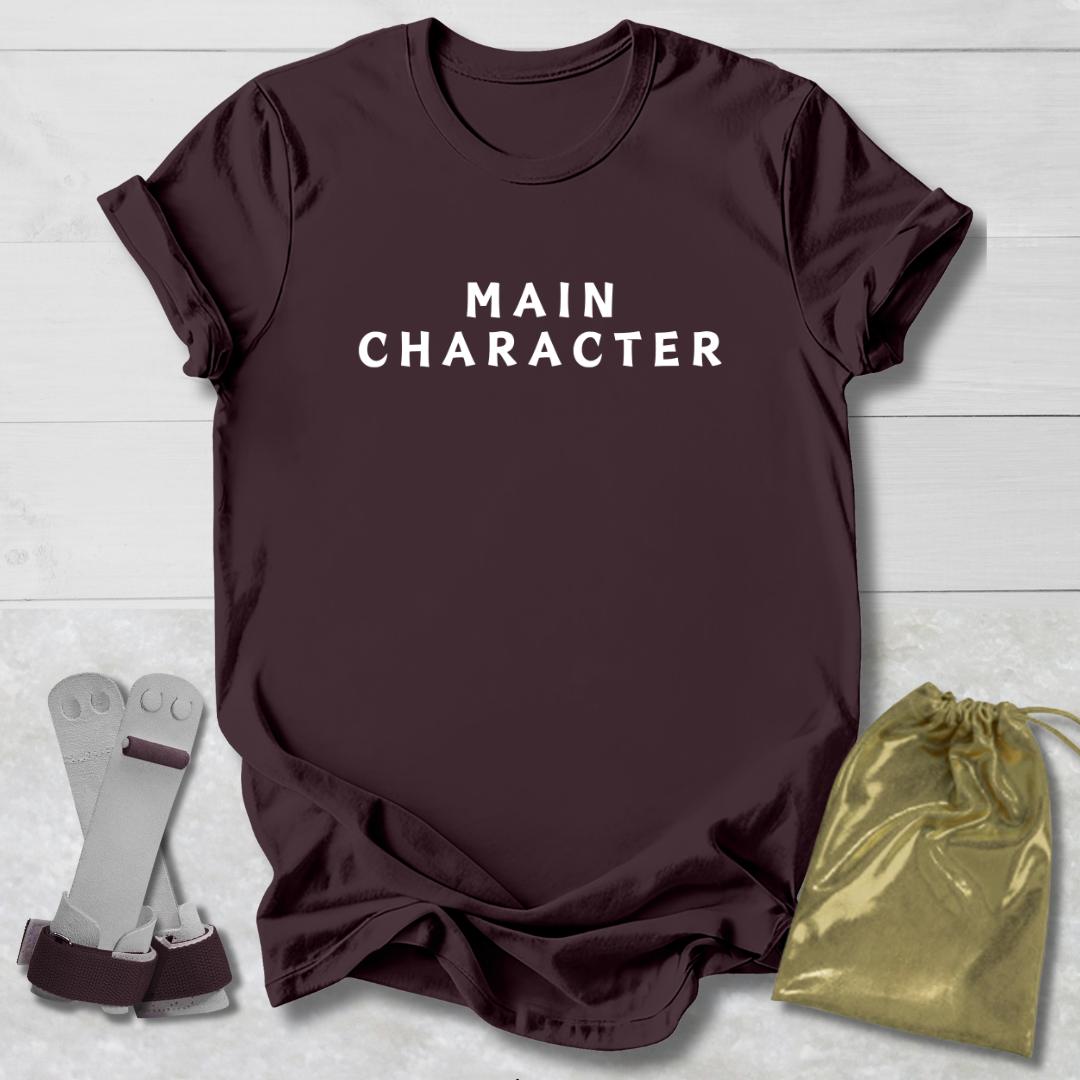 Maroon t-shirt with 'MAIN CHARACTER' text, socks, and drawstring bag on a light wooden surface