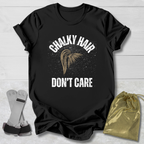 Black t-shirt with 'Chalky Hair Don't Care' text and graphics on a wooden surface.
