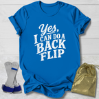 Blue t-shirt with 'Yes, I can do a back flip' text on a light wooden surface with socks and a drawstring bag.