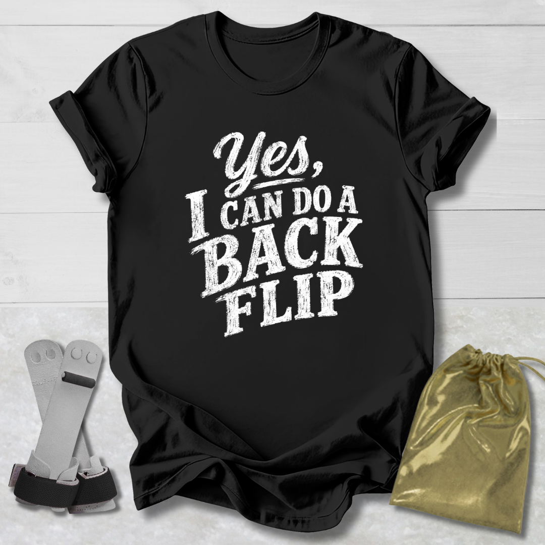 Black t-shirt with 'Yes, I can do a back flip' text on a light wooden surface with socks and a drawstring bag.