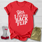 Red t-shirt with 'Yes, I can do a back flip' text, socks, and drawstring bag on a light wooden surface.