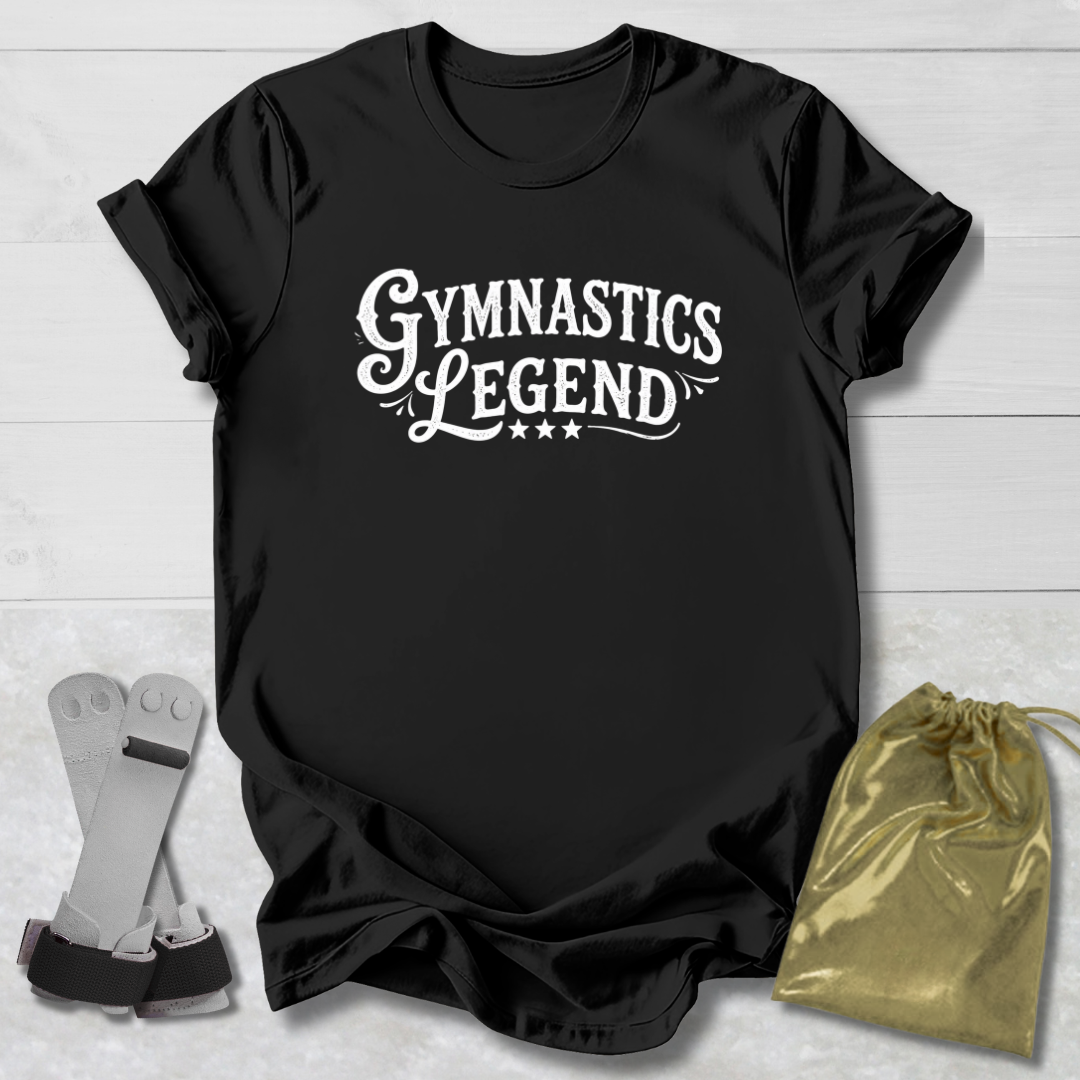 Black t-shirt with 'Gymnastics Legend' text on a light wooden surface with socks and a drawstring bag.