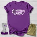 Purple t-shirt with 'Gymnastics Legend' text, gray socks, and gold drawstring bag on a light wooden surface.