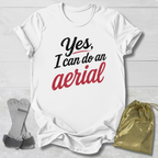 White t-shirt with 'Yes, I can do an aerial' text on a light wooden surface with accessories.