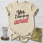 Beige t-shirt with 'Yes, I can do an aerial' text, socks, and drawstring bag on a light wooden surface.