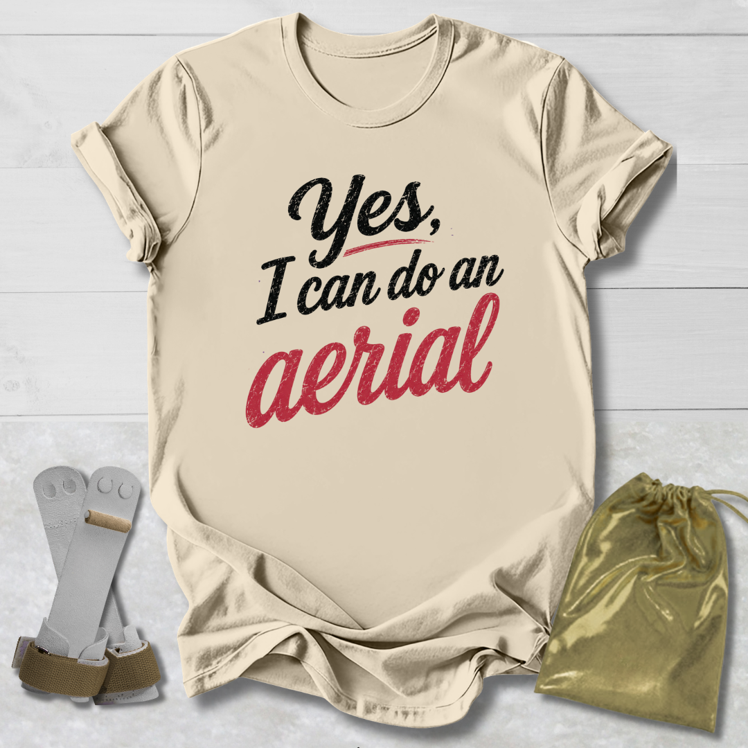 Beige t-shirt with 'Yes, I can do an aerial' text, socks, and drawstring bag on a light wooden surface.