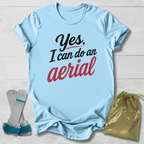 Light blue t-shirt with 'Yes, I can do an aerial' text, socks, and drawstring bag on a wooden surface.