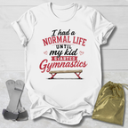 White t-shirt with humorous gymnastics text design on a light wooden surface with socks and a drawstring bag.