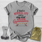 Gray t-shirt with red and black text and graphics, socks, and drawstring bag on a light wooden surface.