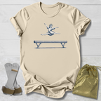Beige t-shirt with a graphic of a gymnast on a balance beam, socks, and a drawstring bag on a light wooden surface.