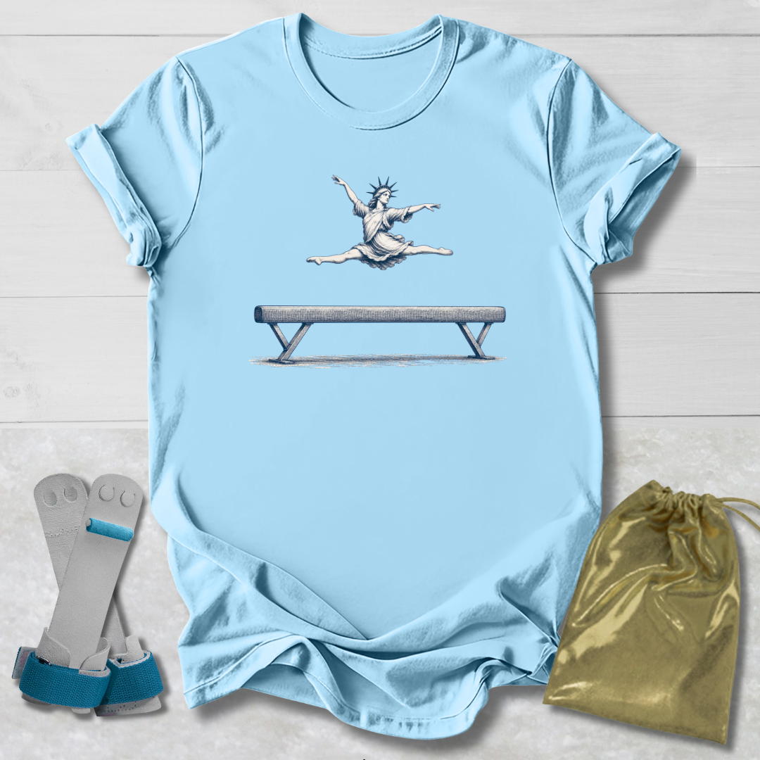 Light blue t-shirt with a graphic of a gymnast on a balance beam, paired with socks and a drawstring bag on a wooden surface.