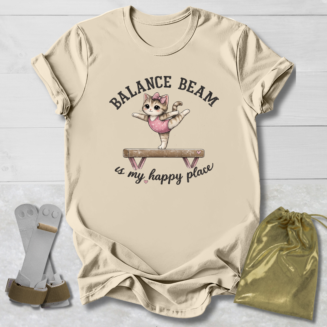 Beige t-shirt with a graphic of a cat on a balance beam and text, placed on a light wooden surface with socks and a drawstring bag.