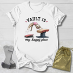 White t-shirt with a graphic design of a cat on a vault and text 'VAULT IS my happy place' on a light wooden surface.