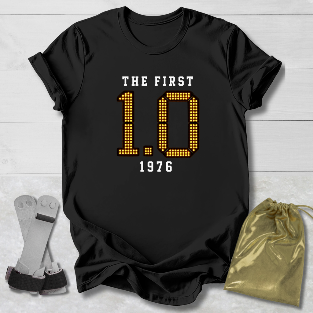 Black t-shirt with 'The First 1.0 1976' text, socks, and drawstring bag on a light wooden surface