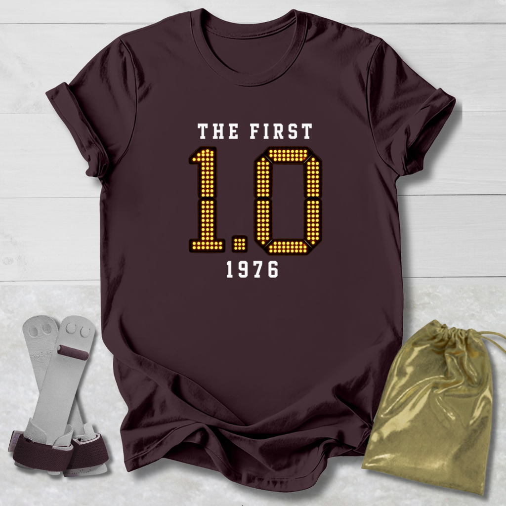 Maroon t-shirt with 'The First 1.0 1976' text, socks, and drawstring bag on a light wooden surface.