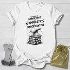 White t-shirt with 'Gymnastics is Importanter' design on a wooden surface with socks and a drawstring bag.