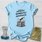 Light blue t-shirt with gymnastics-themed design and text, displayed on a wooden surface with socks and a drawstring bag.