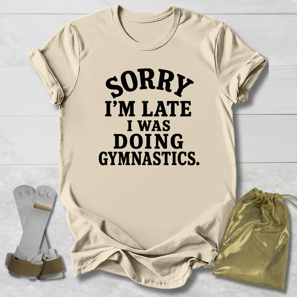 A beige graphic t-shirt with the text 'SORRY I'M LATE I WAS DOING GYMNASTICS.' printed in black.