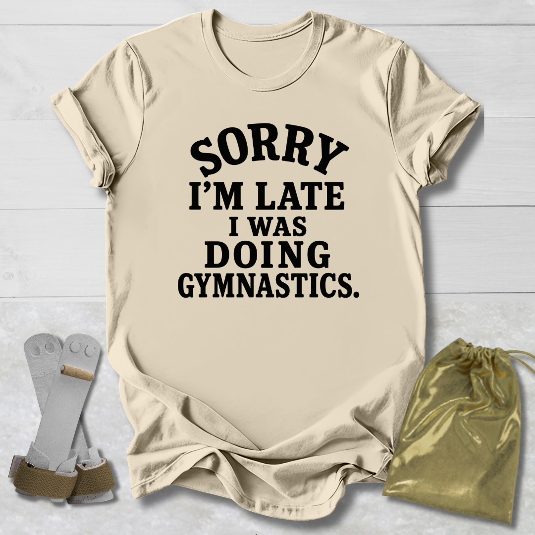 A beige graphic t-shirt with the text 'SORRY I'M LATE I WAS DOING GYMNASTICS.' printed in black.