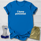A bright blue short-sleeve T-shirt with the phrase 'i have potential' printed in white across the chest, laid flat on a light wood background. A gold drawstring pouch and a pair of gray-and-blue wrist/ankle wraps are placed beside the shirt as included accessories or styling props.