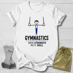 A white short-sleeve graphic T-shirt laid flat on a light wood background, featuring a gymnastics stick-figure illustration and the text 'GYMNASTICS WHERE STRENGTH MEETS SKILL.' A gray gymnastics strap and a gold drawstring pouch are placed beside the shirt as styling props.