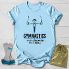 A light blue graphic t-shirt laid flat on a white wood background, featuring a gymnast hanging from rings and the text 'GYMNASTICS WHERE STRENGTH MEETS SKILL'. A pair of gymnastics bars and a gold drawstring bag are placed beside the shirt as styling props.